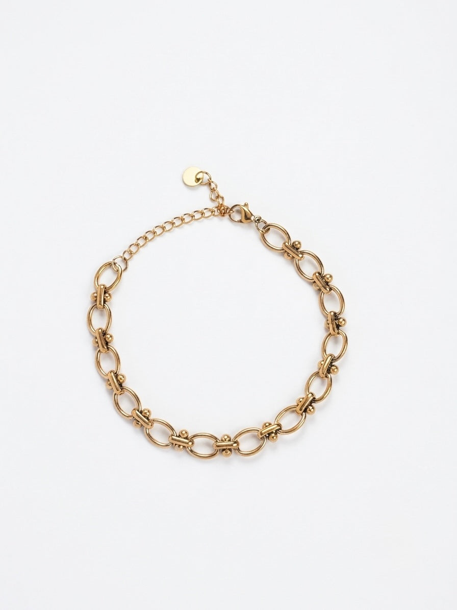 A gold-toned metal chain link bracelet with elongated oval links and a small extender chain with a round tag, shown on a plain white background.