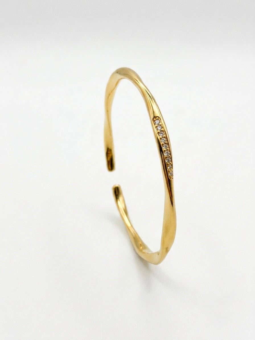 A polished gold open cuff bracelet with a curved row of small clear stones along one side, photographed on a clean white background.