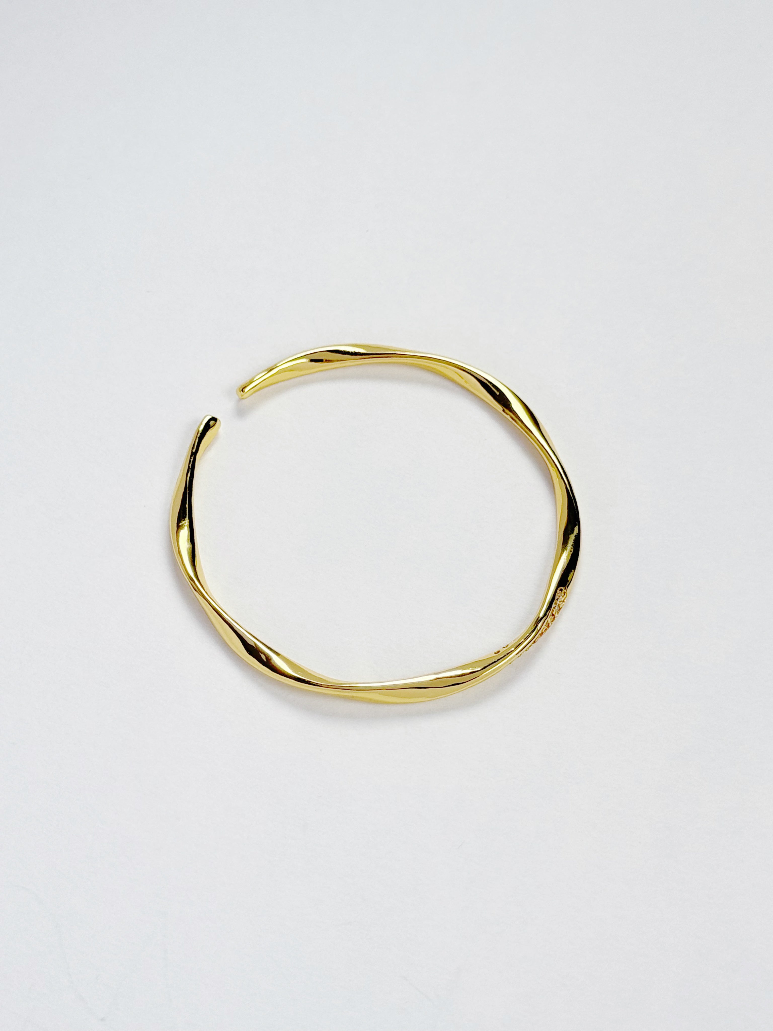 A twisted open cuff bangle in polished yellow gold, photographed on a clean white background.