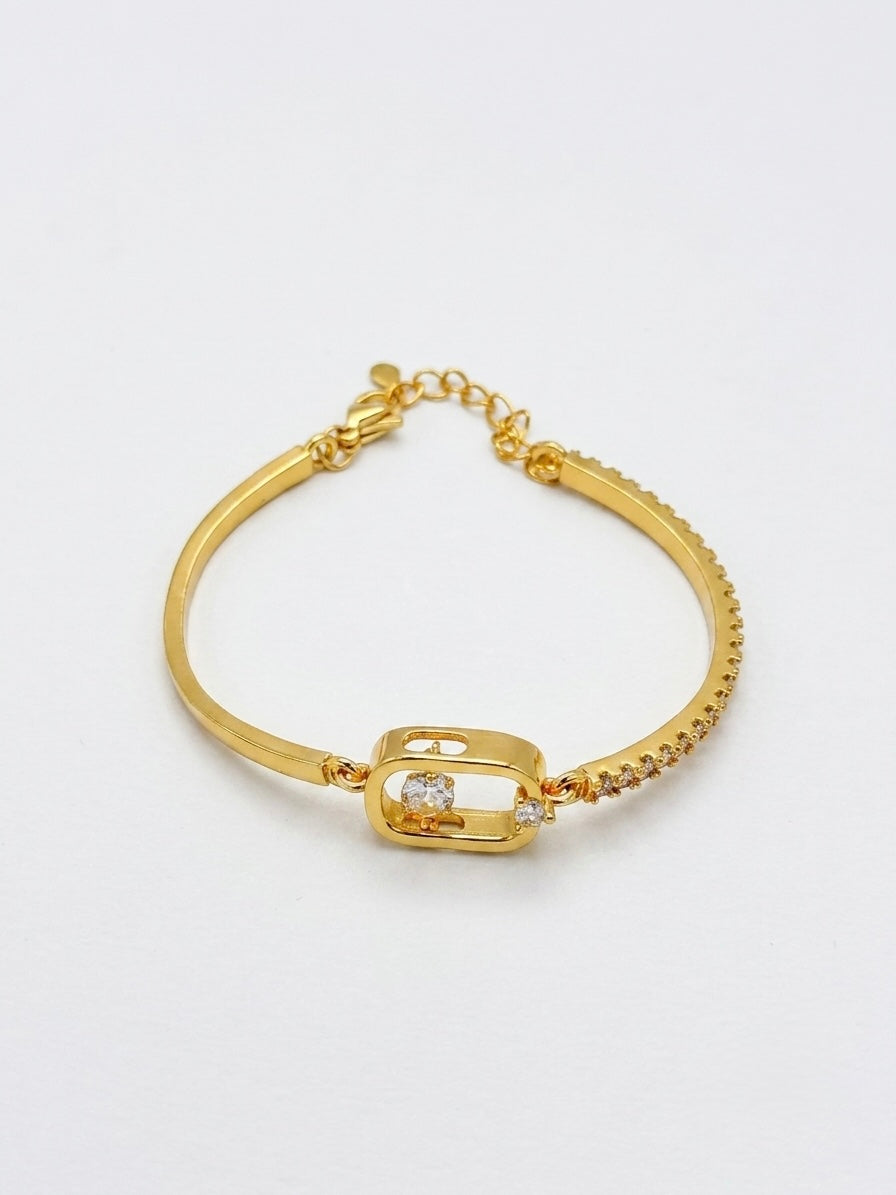A gold-plated bangle bracelet with a central rectangular frame holding a clear rhinestone, accented with small pavé-set stones along the curved sides, shown on a plain white background.