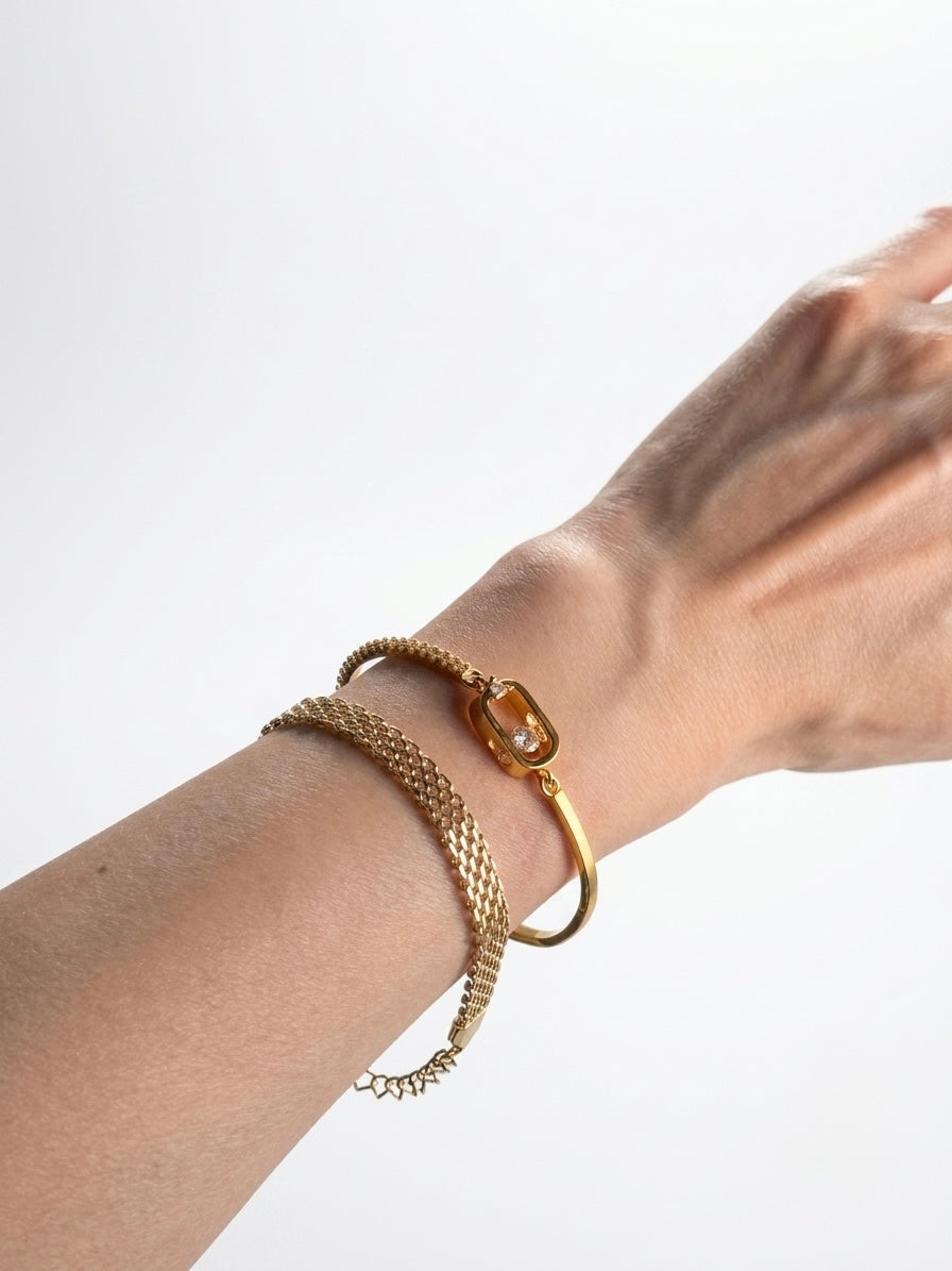 A close-up of a person's wrist wearing three gold-toned bracelets against a plain light gray background.