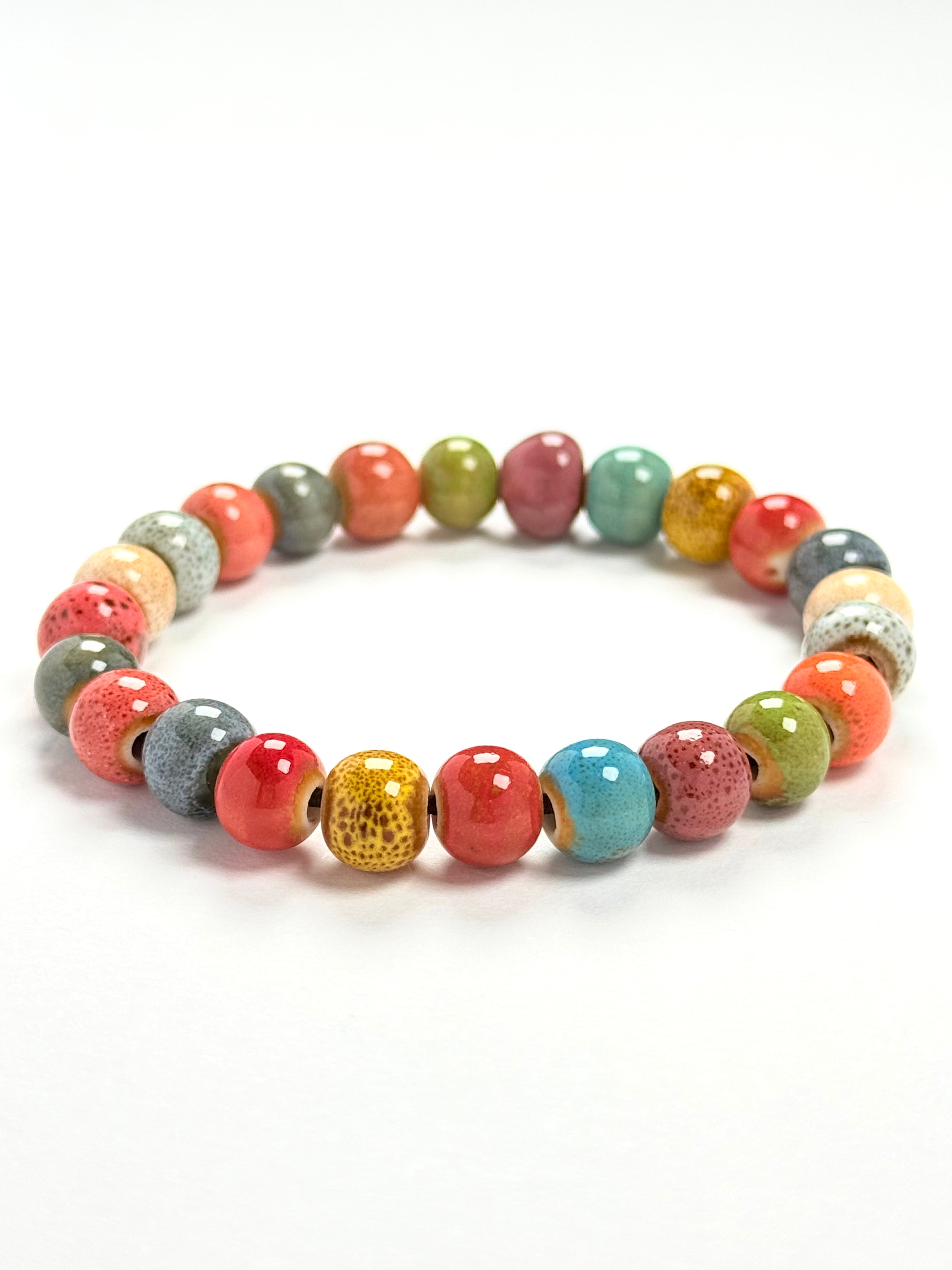 A beaded stretch bracelet made of round, glossy ceramic beads in a variety of colors including coral red, turquoise blue, olive green, pink, gray, and gold speckled finish, displayed on a clean white background.