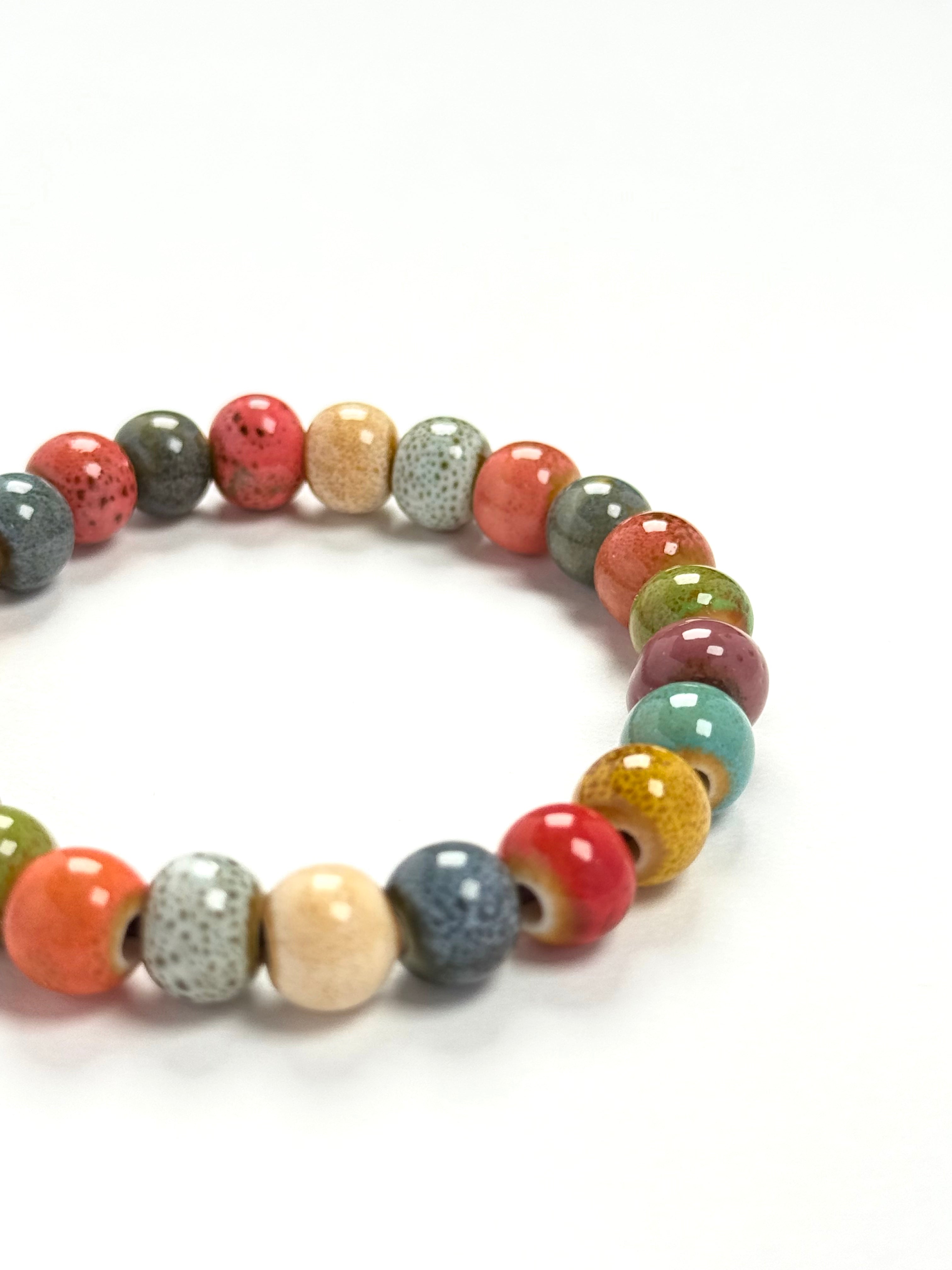 A beaded stretch bracelet made of glossy, round ceramic beads in a variety of colors including orange, red, green, blue, yellow, and speckled gray, arranged in a circle on a white background.