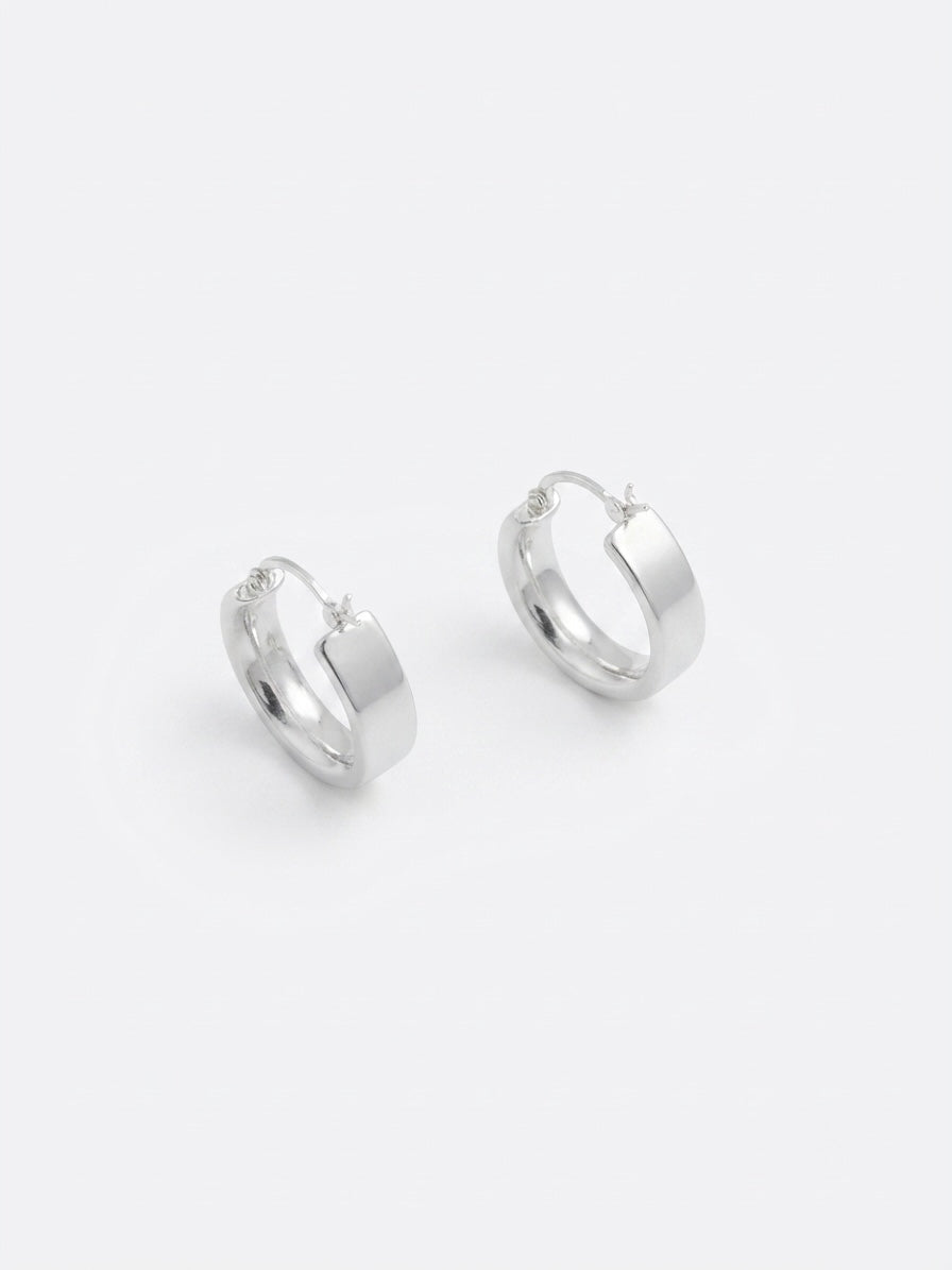 A pair of polished silver huggie hoop earrings on a clean, light gray background.