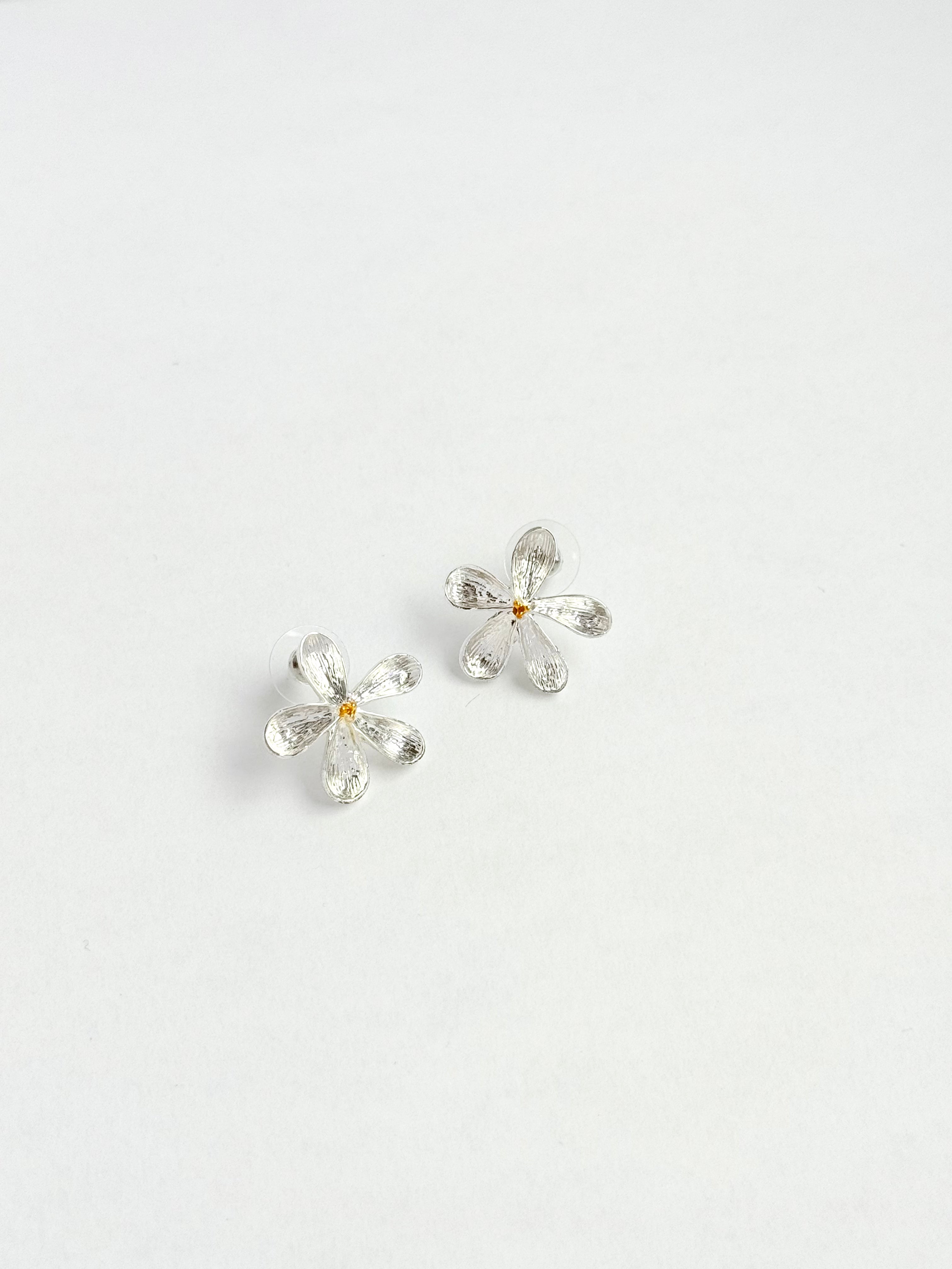 A pair of silver flower-shaped stud earrings with a small gold center, displayed on a clean white background.