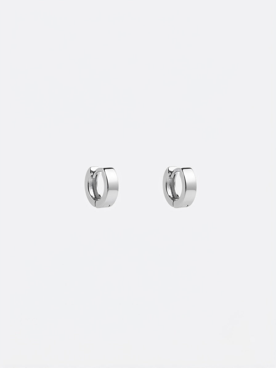 A pair of polished silver huggie hoop earrings on a light gray background.