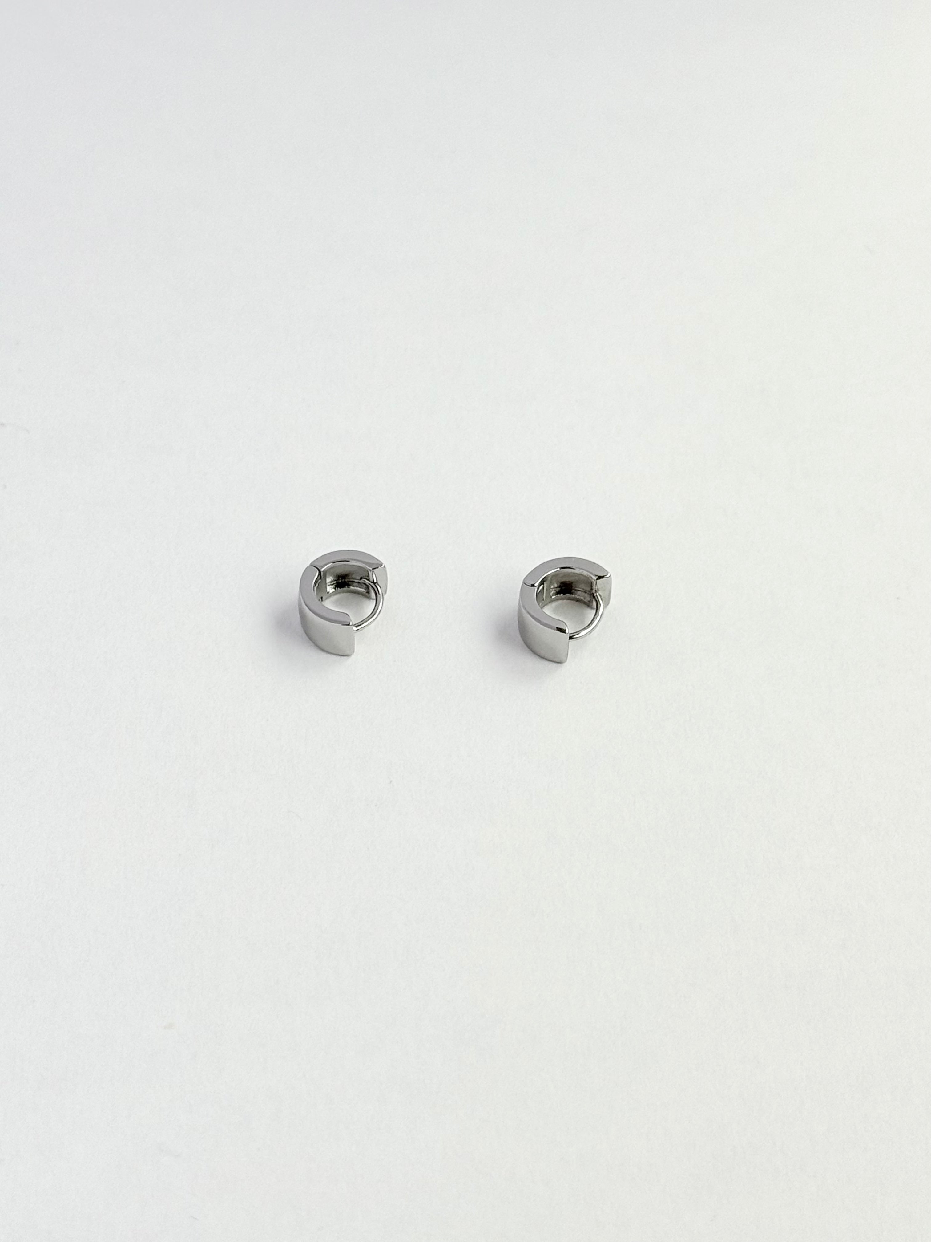 A pair of small silver-toned metal hoop earrings with a slightly curved, organic shape, displayed on a clean white surface.