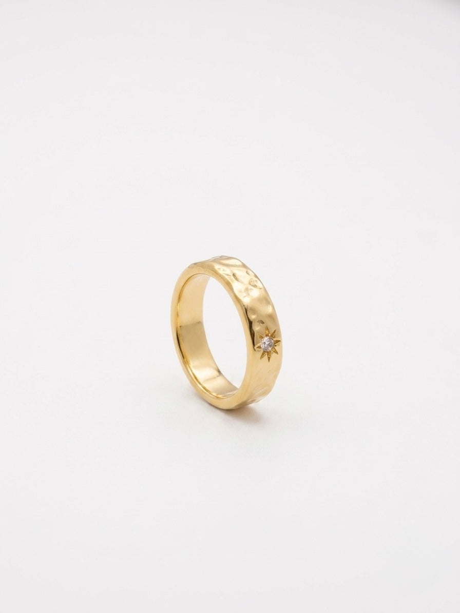 A textured yellow gold band ring with a small starburst detail and a tiny clear gemstone.