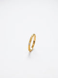 A delicate gold band ring with a textured, hammered finish and a small clear gemstone set near the front, photographed on a seamless white background.