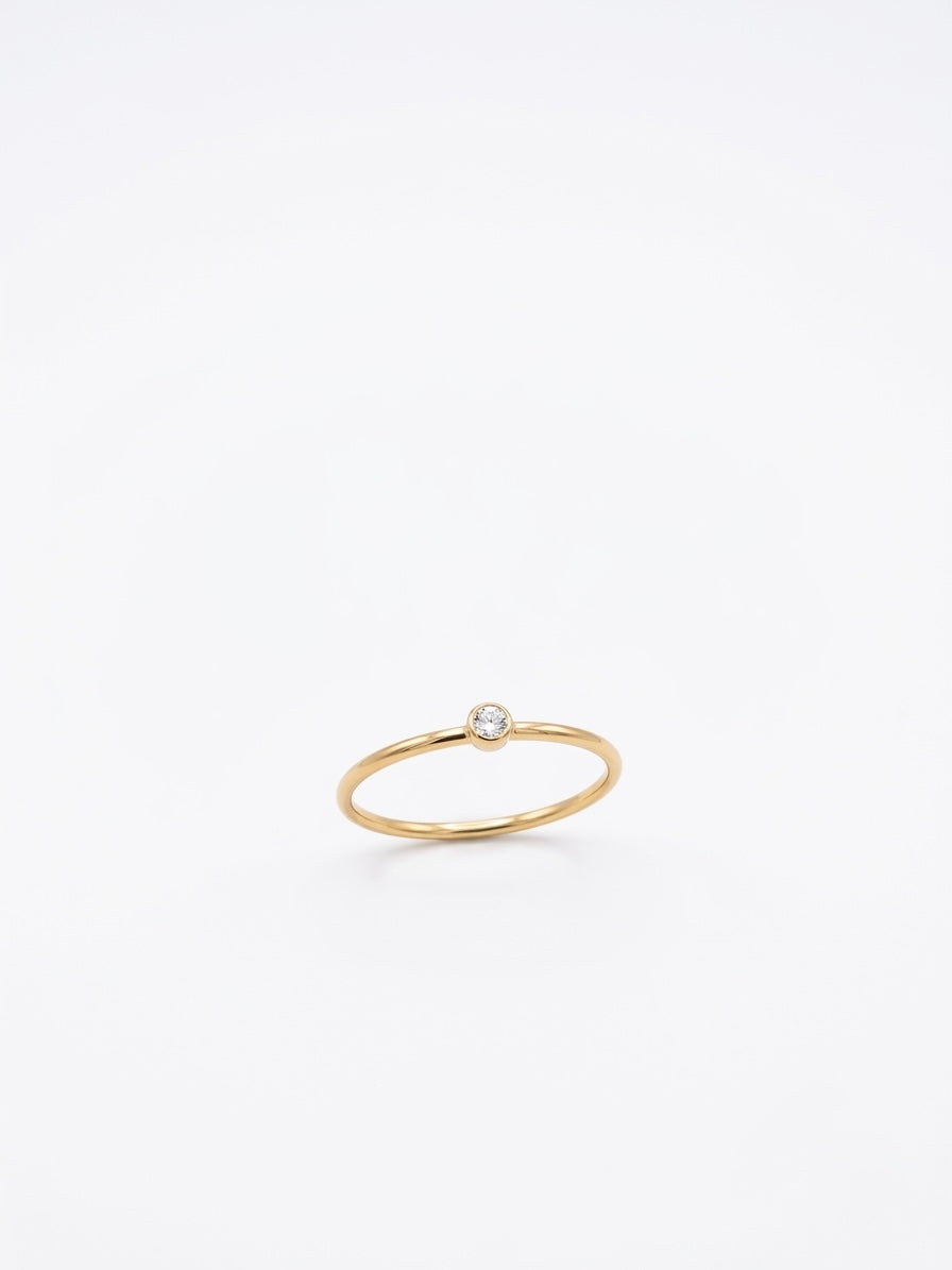 A delicate gold ring with a single small clear gemstone, photographed on a seamless white background.